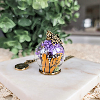 Pendentif porte-bonheur fait avec de vraies fleurs et aile de papillon monarque dans un globe soufflé style antique bronze laiton