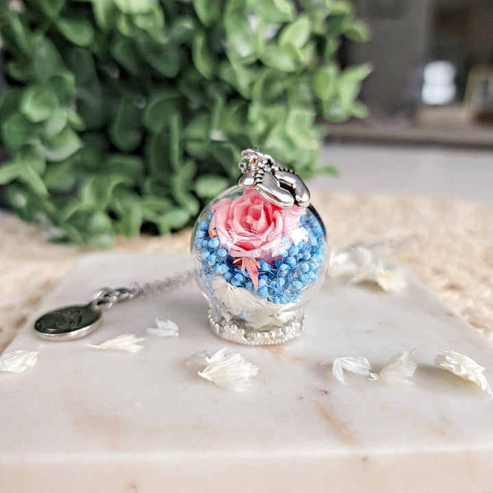 Collier floral avec fleurs naturelles et breloque pieds de bébé, symbole doux du périnatal et de l’amour éternel.