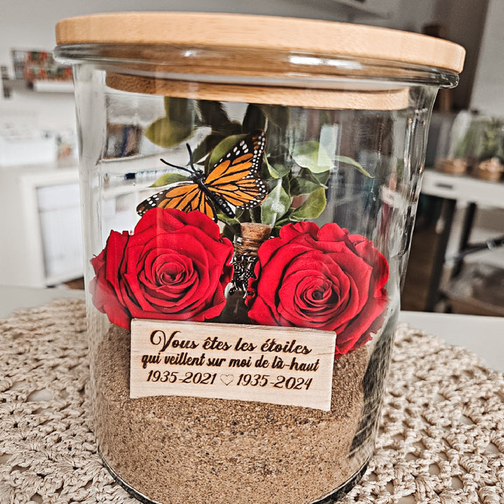 Arrangement floral personnalisé en hommage à un être cher, avec rose éternelle, papillon et plaque gravée dans un vase souvenir.