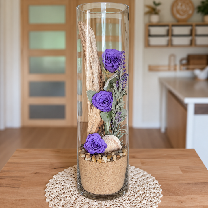 Arrangement floral avec roses éternelles violettes, bois flotté et feuillage dans un grand vase cylindrique