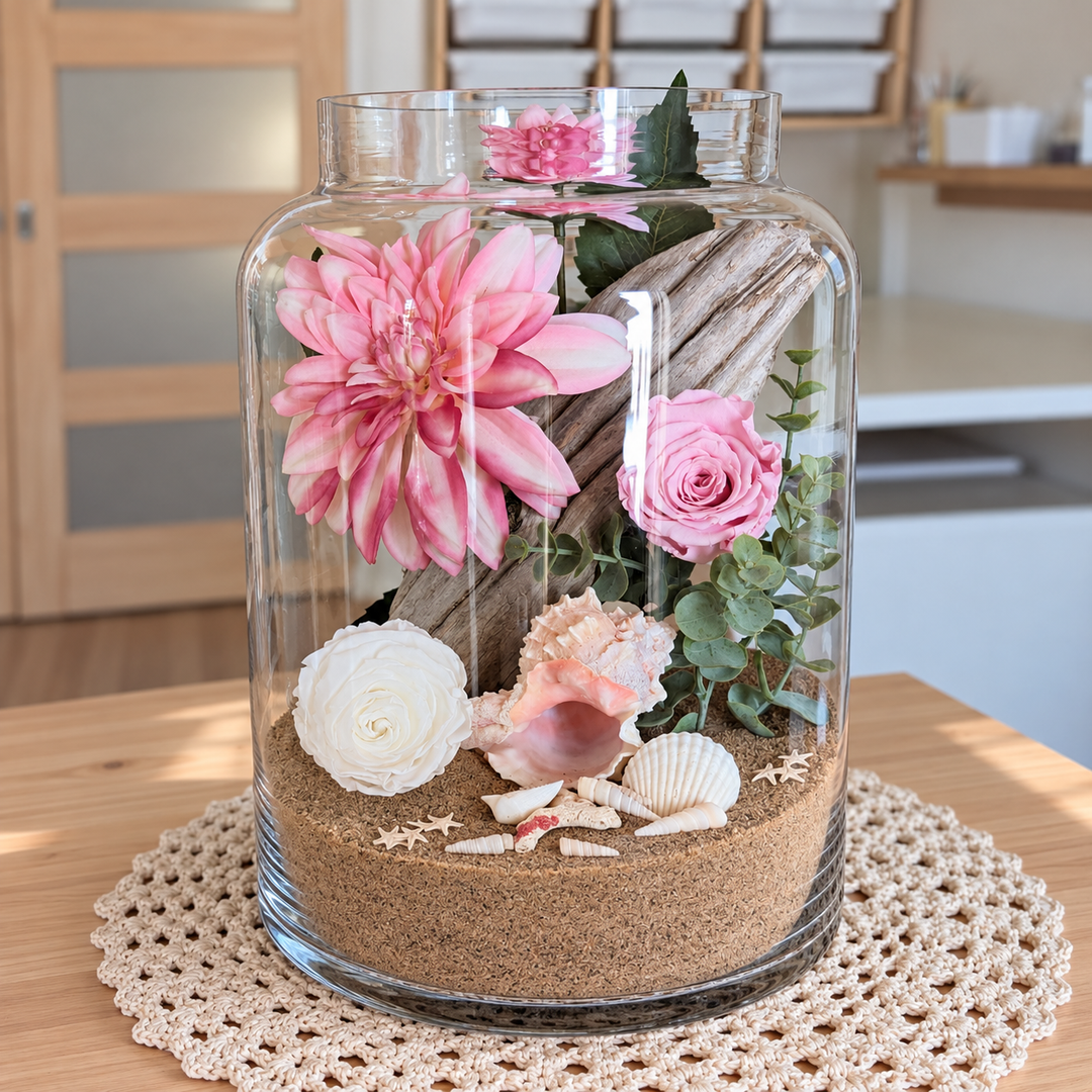 Arrangement floral avec roses éternelles roses et blanches, bois flotté, sable et coquillages