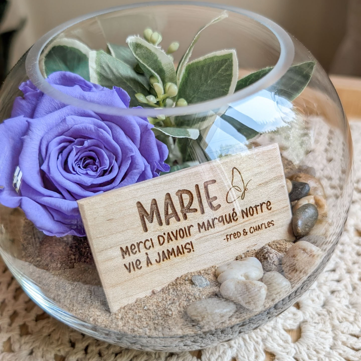 Arrangement avec rose éternelle violette et plaque gravée d’un papillon, offert en cadeau pour remercier un professeur.