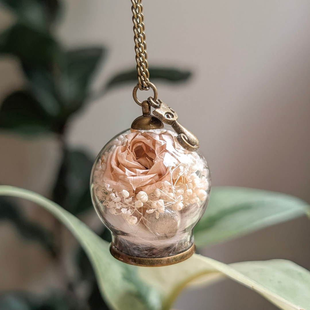 Bijou commémoratif réunissant poils et cendres d’un chat dans un globe de verre avec rose éternelle rose pâle