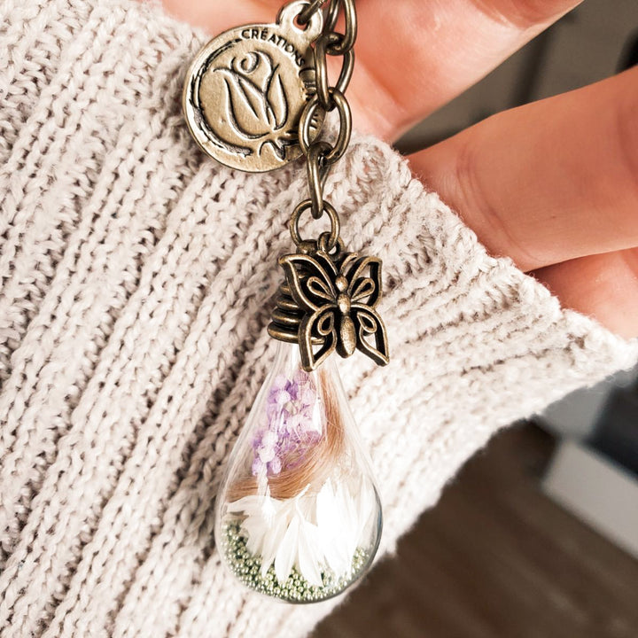 Bijou souvenir avec mèche de cheveux dans verre soufflé et fleurs aux tons doux