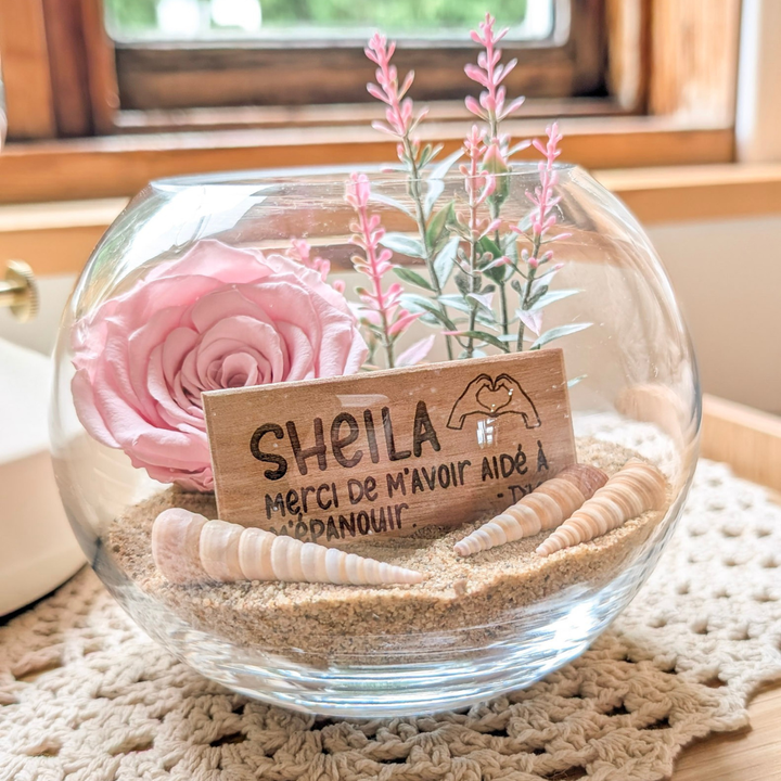 Décoration florale avec rose éternelle rose, coquillages et plaquette gravée au prénom d’une éducatrice.