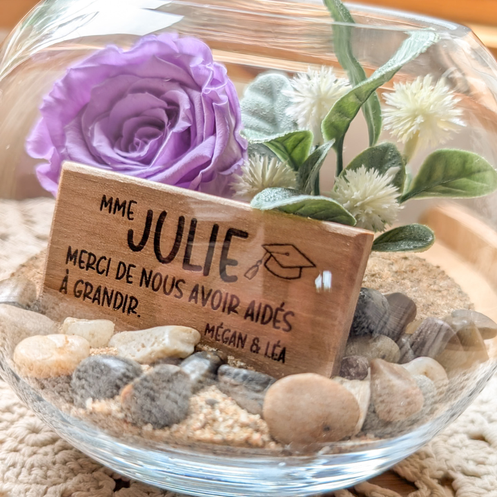 Composition florale avec rose éternelle mauve et plaque de bois personnalisée, offerte comme cadeau à un professeur.