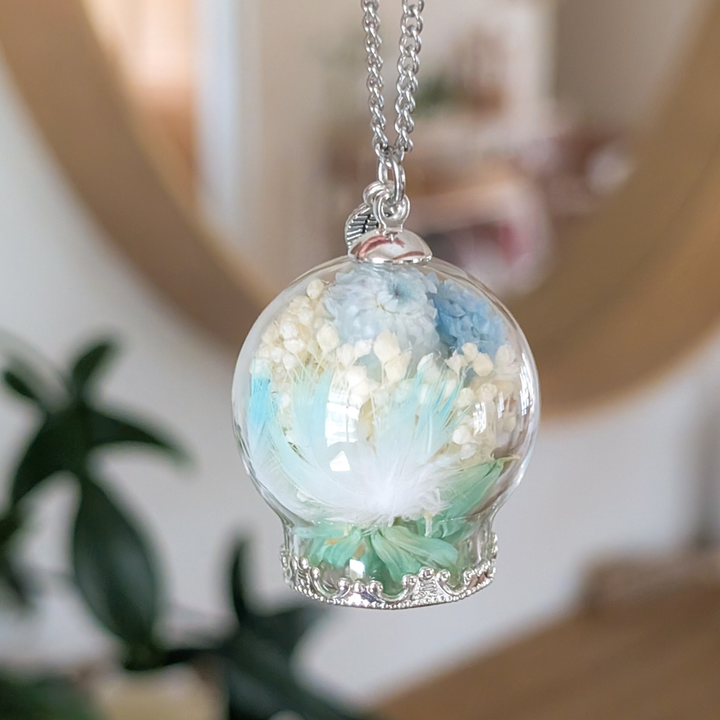 Collier souvenir en boule de verre avec plumes de perruche, fleurs séchées et chaîne en acier inoxydable.