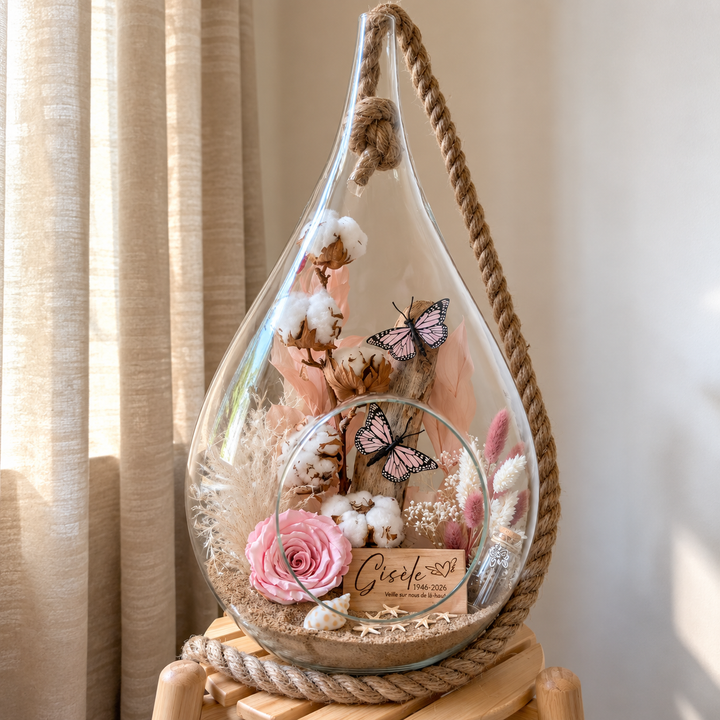 Arrangement floral hommage avec rose éternelle rose, papillons, fleurs de coton et plaquette gravée