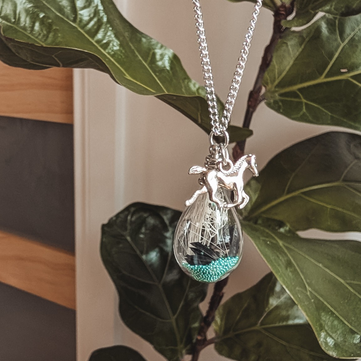Pendentif avec crins de cheval, billes turquoise et breloque cheval, présenté sur une chaîne argentée.