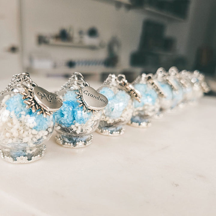 Pendentif souvenir avec mèche de cheveux de grand-maman et fleurs séchées bleues.