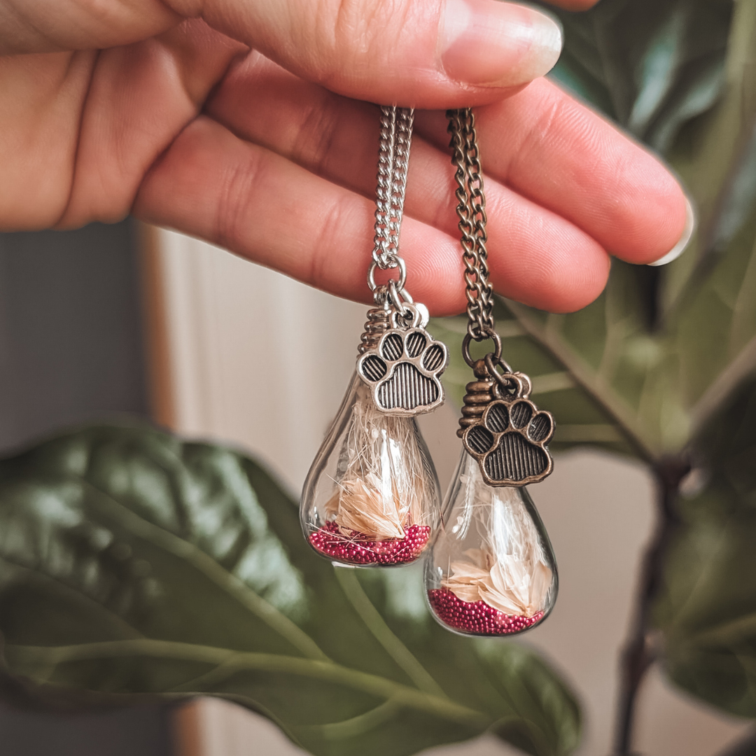 Deux pendentifs souvenir avec poils de chien, fleurs roses et breloques pattes en acier argenté et bronze antique