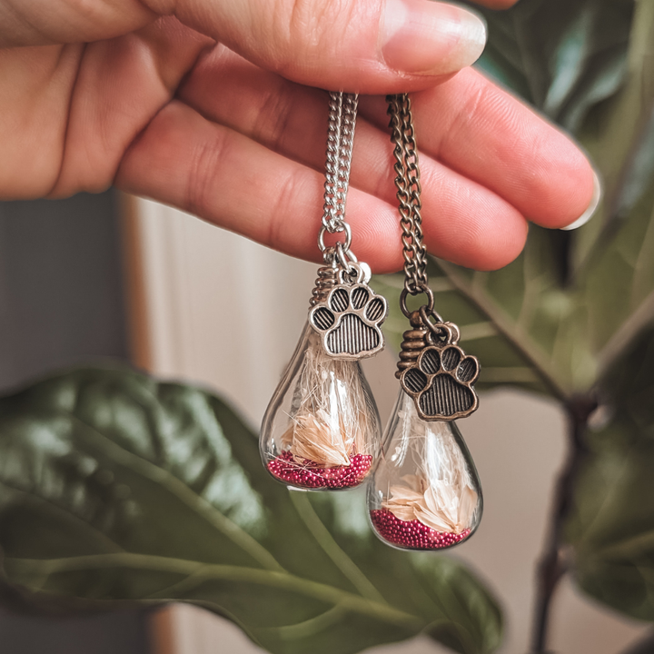 Deux pendentifs souvenir avec poils de chien, fleurs roses et breloques pattes en acier argenté et bronze antique