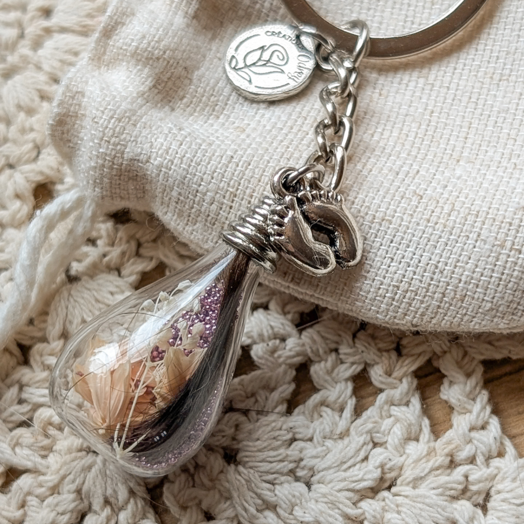 Porte-clé souvenir en goutte de verre avec une mèche de cheveux de bébé, une fleur pêche et une breloque petits pieds