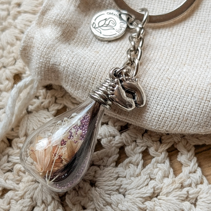Porte-clé souvenir en goutte de verre avec une mèche de cheveux de bébé, une fleur pêche et une breloque petits pieds